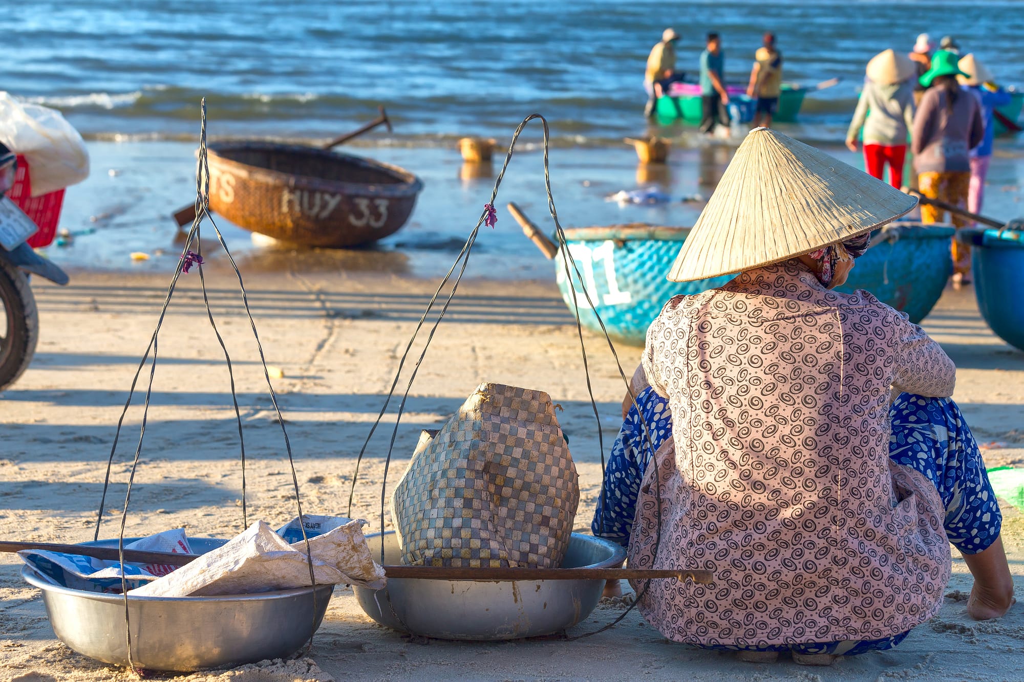 Binh Thuan, Vietnam - January 21st, 2016: Woman with shoulder alignment is waiting for fishermen to bring the beach to buy fish for sale in the morning market in the fishing village of Binh Thuan, Vietnam